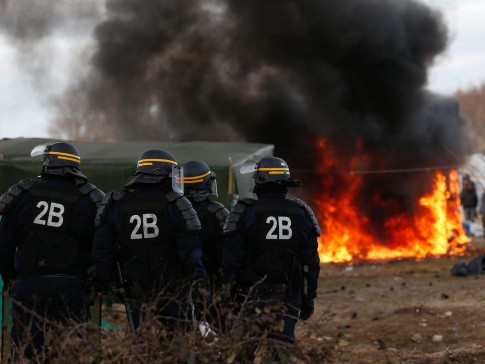 French riot police in front of a burning shelter at the start of the demolition of a part of the Jungle migrant camp in Calais, France, 29 February 2016